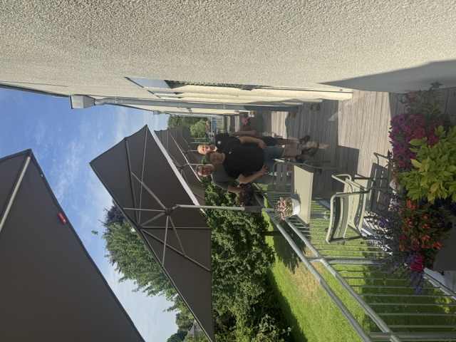 Drei Männer unter Sonnenschirmen auf dem Balkon des Hospiz